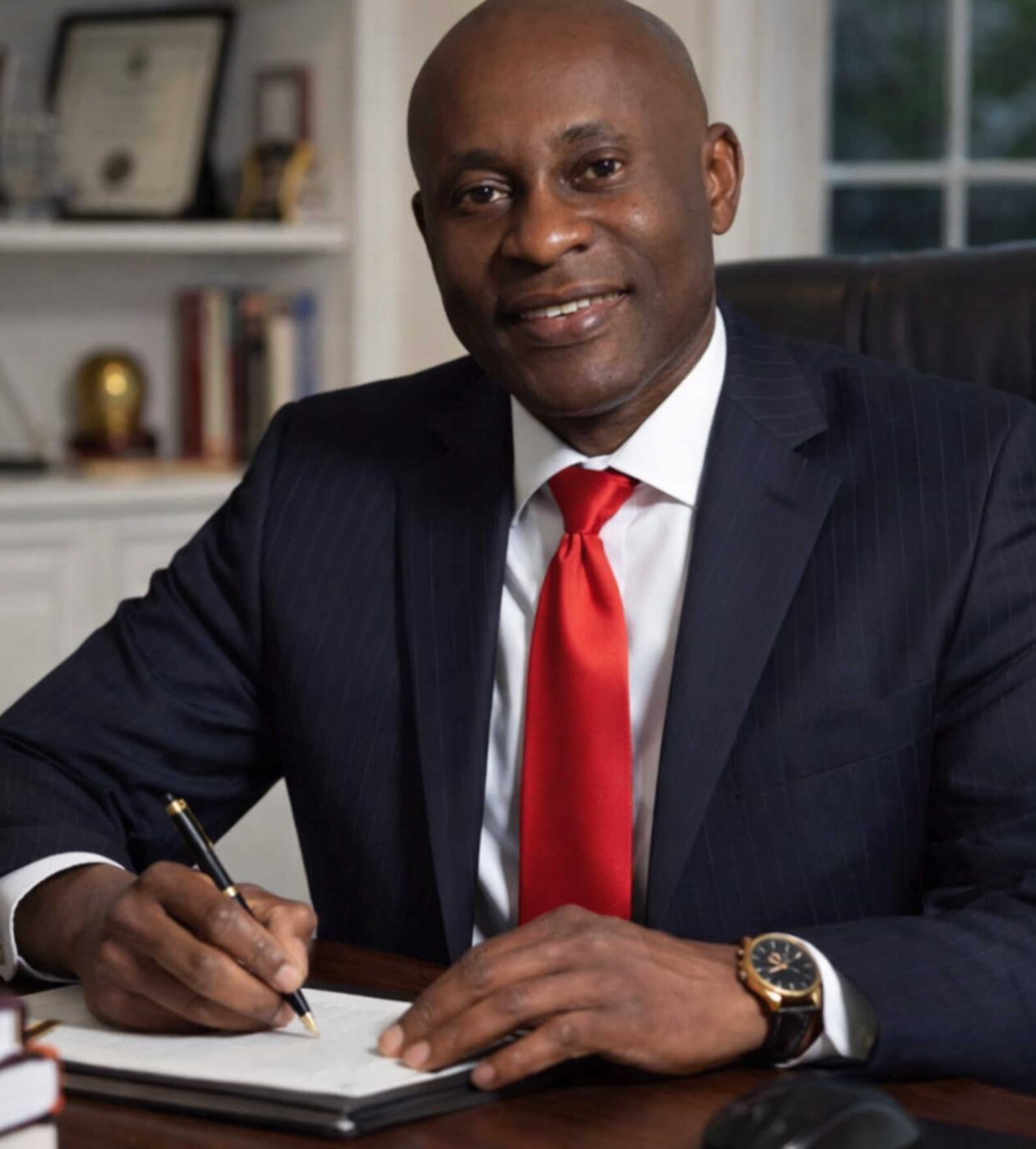 Dr. Obasi, cosmetic surgeon in Plano, TX, seated in office wearing a navy suit and red tie