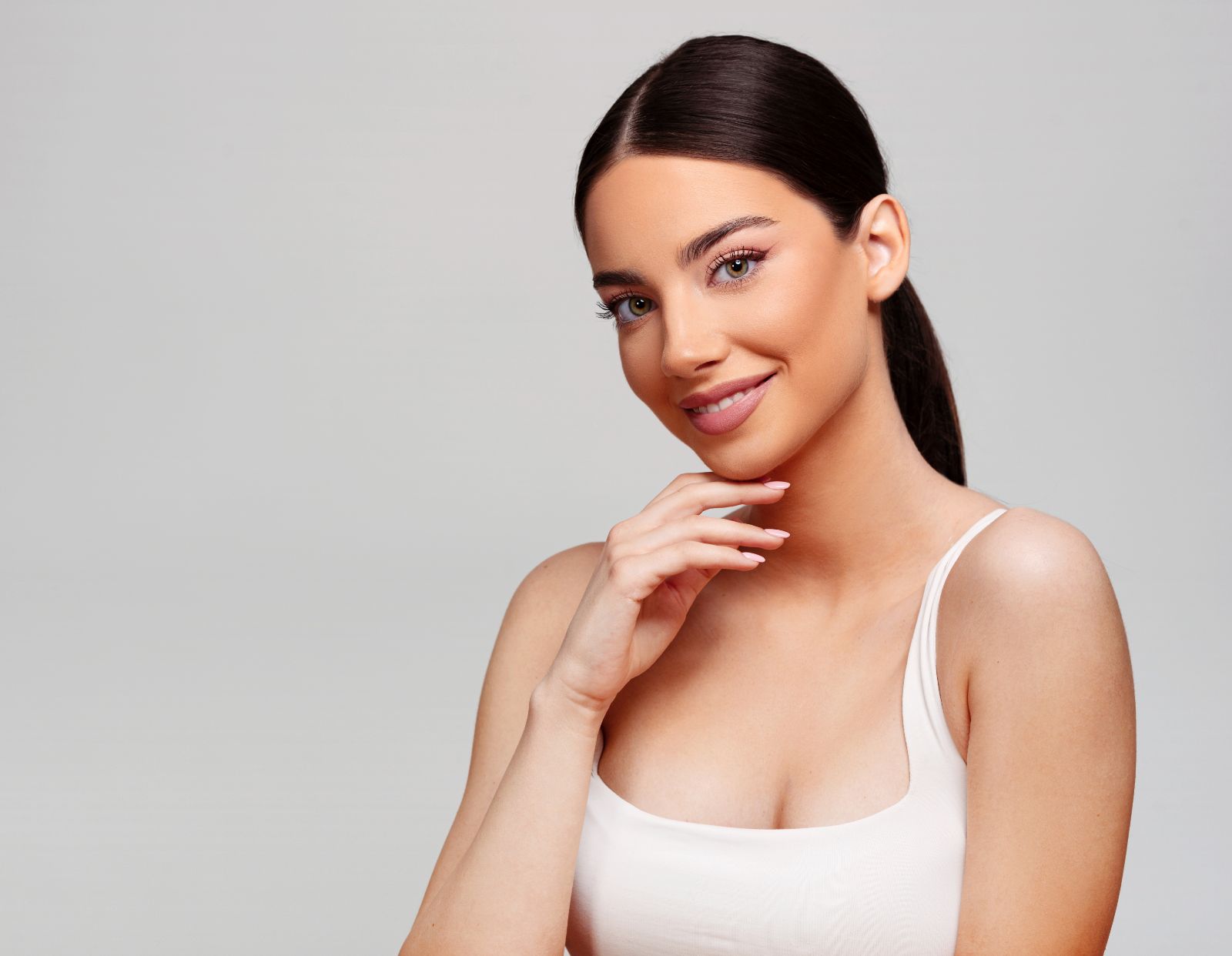 woman touching her chin with beautiful skin, wearing a white top, against a white background