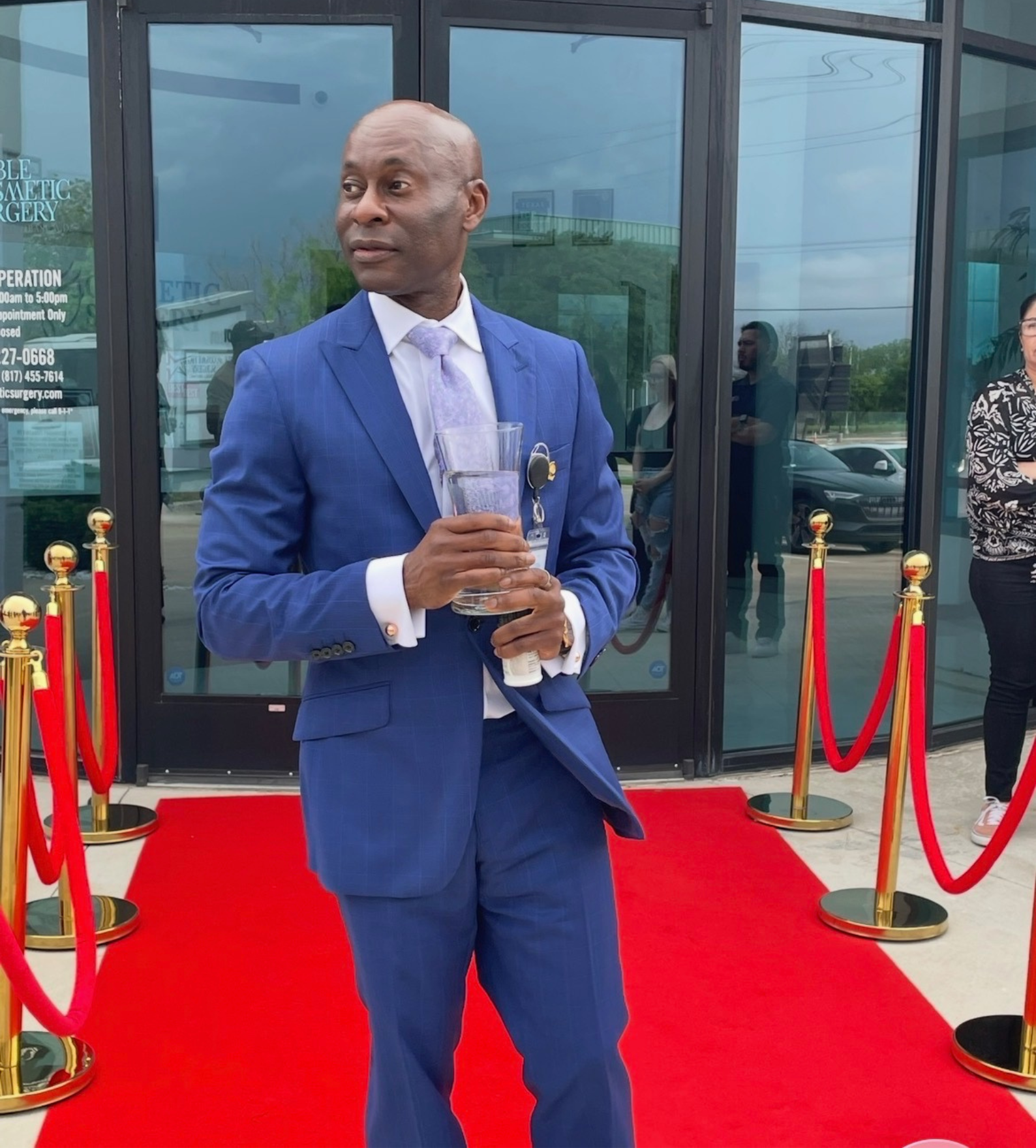 Dr. Patrick C. Obasi standing on a red carpet outside Noble Cosmetic Surgery in Plano, TX, holding an award and smiling in formal attire.