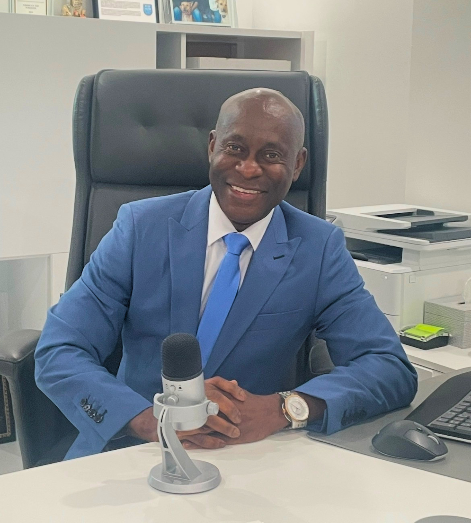 Dr. Patrick C. Obasi sitting at his desk with a microphone, recording a podcast at Noble Cosmetic Surgery in Plano, TX.