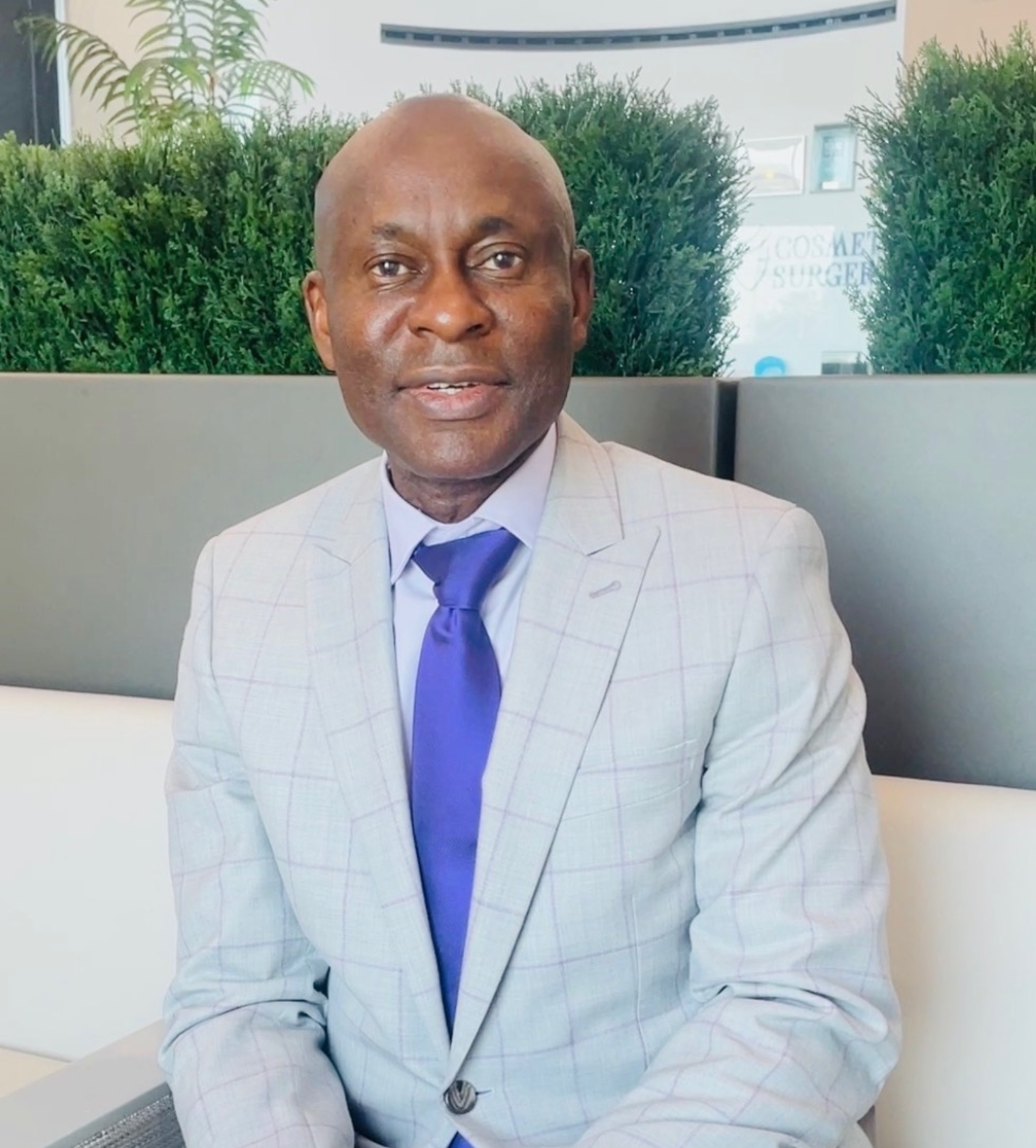 Dr. Patrick C. Obasi seated in the modern lobby of Noble Cosmetic Surgery in Plano, TX, welcoming patients in a luxury setting.